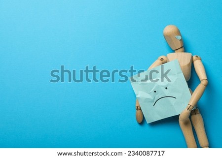 Wooden man with paper with a sad emoji on blue background, space for text