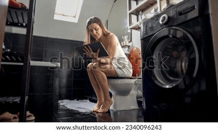 A woman multitasking, sitting on a toilet, and working on a tablet computer. Importance of being efficient and productive in all situations
