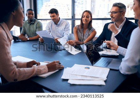 Multi-Cultural Business Team Meeting Around Office Boardroom Table With Laptops Discussing Documents Royalty-Free Stock Photo #2340113525