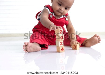 African baby girl in red cloth sitting on floor playing with wooden blocks, wooden blocks with 2024 Number, happy new year