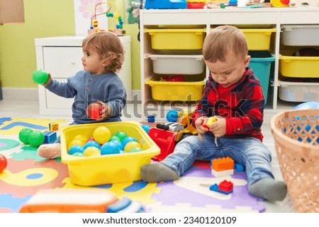 Adorable boys playing with balls and construction blocks sitting on floor at kindergarten