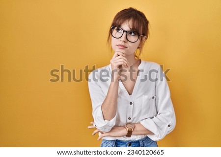 Young beautiful woman wearing casual shirt over yellow background with hand on chin thinking about question, pensive expression. smiling with thoughtful face. doubt concept.  Royalty-Free Stock Photo #2340120665