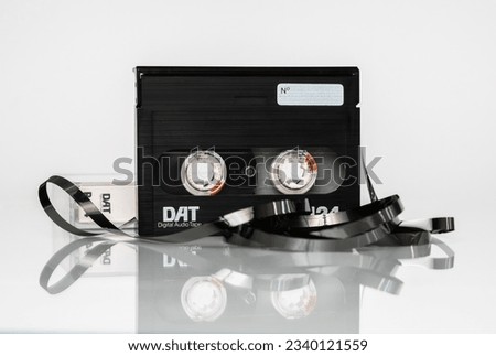 Front view of a DAT (digital audio cassette) cassette with a box and a twisted tape stands upright on a white background with reflection