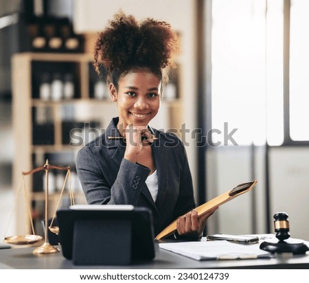 African american lawyer woman in suit holding envelope of business contract and reading information on tablet while sitting to working about legal and justice with judge hammer on desk in courtroom. Royalty-Free Stock Photo #2340124739