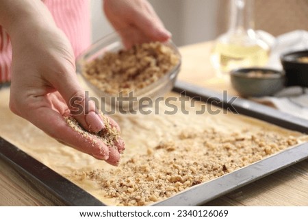 Making delicious baklava. Woman adding chopped nuts to dough at wooden table, closeup Royalty-Free Stock Photo #2340126069