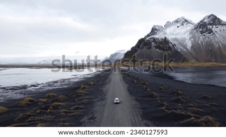 Aerial view of Vestrahorn mountain with snow and a car on the road, on the black sand beach in winter on the Stokksnes peninsula, Iceland