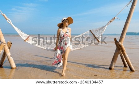 Happy woman standing from lounge hammock at sea beach and walking through the beach with ocean view. Vacation on Phuket island, Thailand. Slow motion. Concept of joyful beach vacation and leisure.