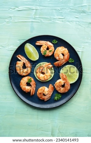 Shrimps, shot from the top on a teal blue background. Cooked shrimp with lime, spicy seafood dish