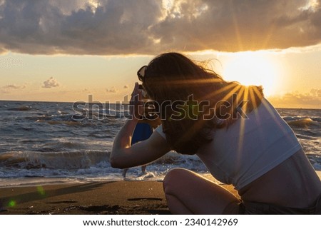 A girl photographs her friend on a mobile phone against the backdrop of a beautiful sunset