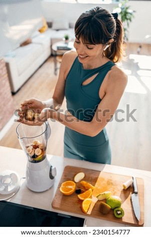 Shot of beautiful sporty woman doing healthy smoothie while listening to music in the kitchen.