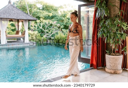 Full length of female traveler in bikini looking down and thinking while chilling on poolside on tropical resort on summer vacation