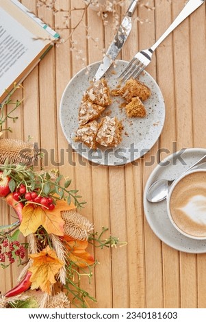 Atmospheric time for yourself - coffee time outside with a book - cutting doughnut and cappuccino among fall decorations. Atmospheric coffee time, guilty pleasure Royalty-Free Stock Photo #2340181603