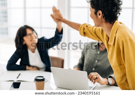 Female colleagues celebrating success in an office. Business women doing a high five during a meeting in a boardroom. Teamwork and goal achievement. Royalty-Free Stock Photo #2340195161