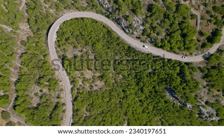 AERIAL TOP DOWN: Cars drive along winding road through rugged Adriatic landscape. Scenic asphalt roadways carved into stone landscape and surrounded with green pine trees on sunny island of Hvar.