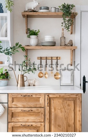 detail in kitchen with scandinavian interior. wooden cabinet, clean plates and bowls on shelves, houseplant in pitcher, utensils on wall and picture with copy space on white countertop