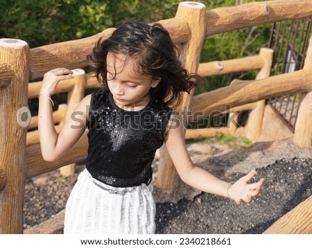 Portrait photo of minded dreamy young little girl. Look empty space hold hand chin isolated on blur background. Wearing black and white outdoor in park with present filter effect.