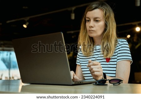 Woman using laptop in coworking with green plants. Female freelancer typing on laptop keyboard. Online work in cafe