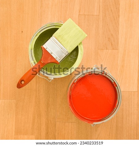 High angle of paintbrush with paint cans on wood floor.