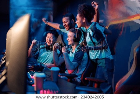 Multiracial cybersport gamers expressing success while raising hands up and smiling during participation in esports tournament in computer club Royalty-Free Stock Photo #2340242005