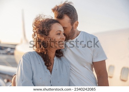 Portrait of lovely couple of tourists, man and woman looking happy while standing outdoors ready for boarding the plane at sunset. Vacation, lifestyle, traveling concept