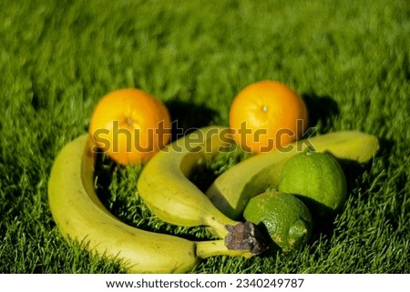 This is a photo-realistic image of three fruits on green grass. The photo has a banana, a lime, and an orange. The banana peel serves as a bowl for the fruits. 