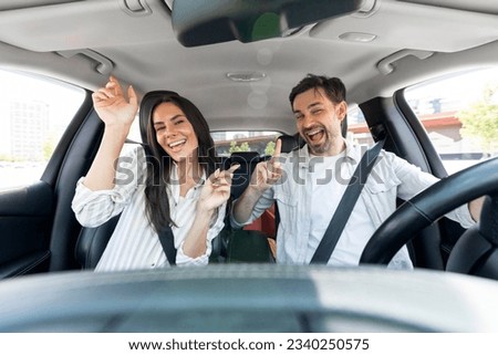 Active leisure, summer vacation, recreation, car trip concept. Funny positive millennial couple husband and wife having fun while driving auto, listening to music and dancing, shot from dashboard Royalty-Free Stock Photo #2340250575