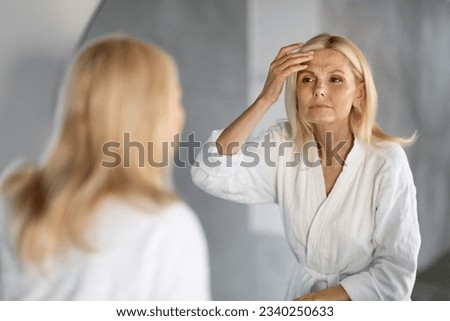 Mature Woman Looking In Mirror And Touching Wrinkles On Her Face, Upset Beautiful Senior Female Examining Fine Lines On Forehead, Suffering Skin Aging, Selective Focus On Reflection, Closeup Royalty-Free Stock Photo #2340250633