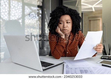 Sad disappointed businesswoman inside office at workplace looking at documents papers financial reports, african american female worker on paper work depressed unhappy with financial achievements Royalty-Free Stock Photo #2340253033