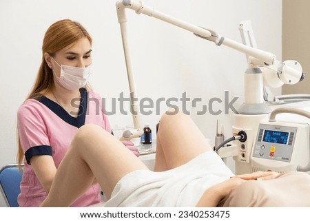 a woman doctor, laser gynecology, makes an operation for a middle-aged patient using a Fotona laser device. The concept of laser technology in gynecology and women's health. Royalty-Free Stock Photo #2340253475