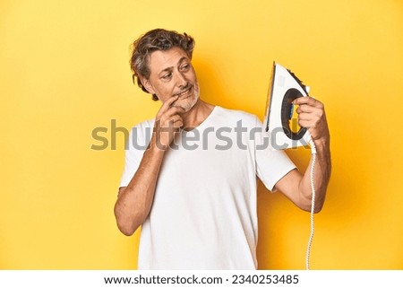 Man with iron in hand on a yellow background relaxed thinking about something looking at a copy space.