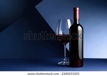 Bottle and glass of red wine on a blue background. Copy space.