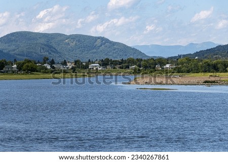 view of a river with houses, mountains under a cloudy sky
