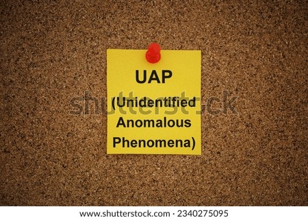 A yellow paper note with the words UAP (Unidentified Anomalous Phenomena) on it pinned to a cork board. Close up. Royalty-Free Stock Photo #2340275095
