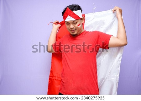 Excited Indonesian man celebrate indonesian independence day on 17 August, wearing red shirt. isolated on purple background. copyspace
