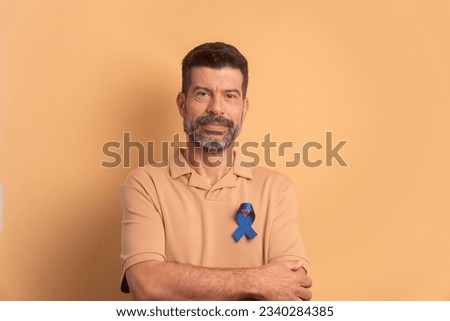 confident caucasian man showing blue ribbon in beige background. prostate cancer, awareness concept. Royalty-Free Stock Photo #2340284385