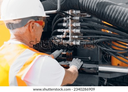 Man in hard hat industrial worker Machinery tractor mechanic checks hydraulic hose system equipment on excavator. Royalty-Free Stock Photo #2340286909