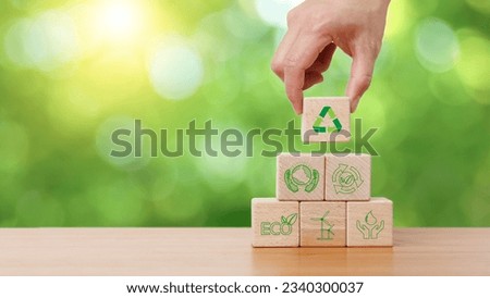 Hand holding wooden cube block with recycle, earth, eco friendly and green energy icon in green background. Sustainable and environmental responsibility concept. Royalty-Free Stock Photo #2340300037