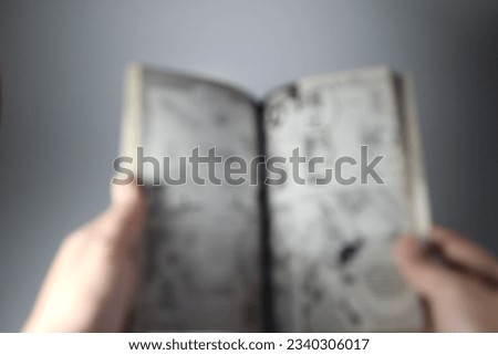 Defocused or blurred image of an adult hands open flip and holding a Japanese comic book or manga. Reading. Bokeh background, isolated on white.