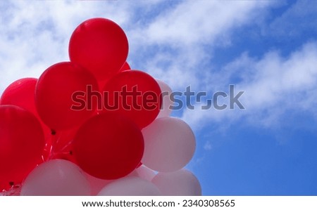 Red and white balloons against a blue sky with clouds. Festive background