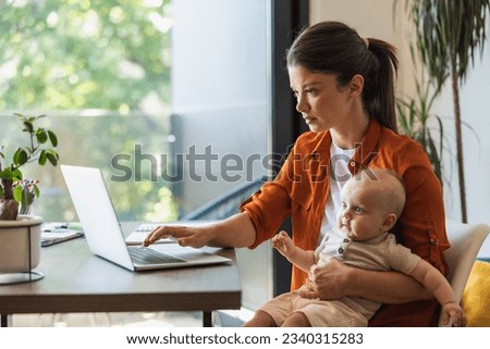 Female entrepreneur working on laptop and taking care of her baby at home. Royalty-Free Stock Photo #2340315283