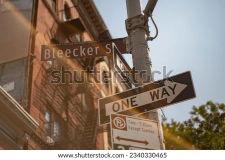 New York city Bleecker Street sign with one way signs, brownstone and light flare