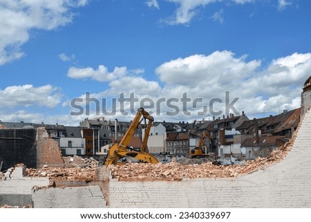 Several construction excavators are engaged in dismantling an old house. Dismantling the city's housing stock for renovation