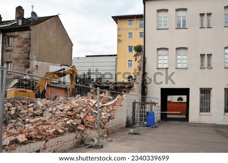 A construction excavator is dismantling an old brick house behind a wire fence. Dismantling the city's housing stock for renovation