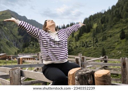 Young woman sitting on fence with her hands raised and her head thrown back, the concept of Escapism, Austria