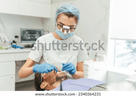 Middle aged bearded man patient with open mouth sitting in dental clinic while skilful female dentist checking his teeth. Somatology concept  Royalty-Free Stock Photo #2340364231