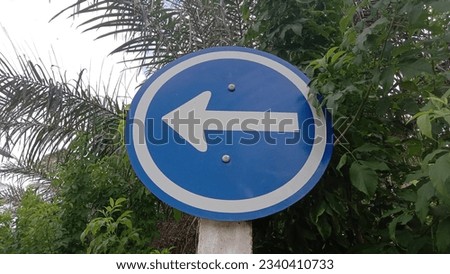 A blue circular road sign with a white arrow pointing to the left.