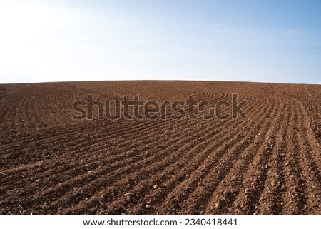 Plowed farmland with brown soil and a blue sunny sky Royalty-Free Stock Photo #2340418441