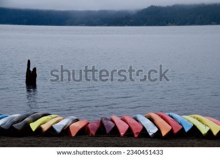 a row of colorful kayaks on the shore of the lake on a foggy morning with mountains in the background Royalty-Free Stock Photo #2340451433
