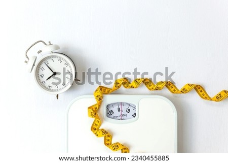 Weight loss control planning.  White scale and measuring tape and timing alarm clock for body dieting healthy life.  White background. Top view copy space for banner Royalty-Free Stock Photo #2340455885