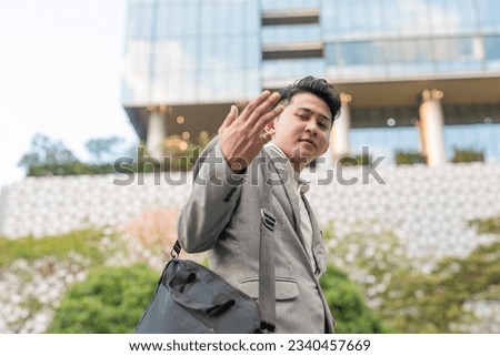 A cocky young asian man tells someone to follow him to the office. Feeling superior or bossy. Outdoor city scene. Royalty-Free Stock Photo #2340457669